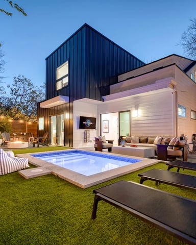 Overhead view of illuminated backyard with two hot tubs, lounge seating, wooden deck, and ivy-covered fences at dusk